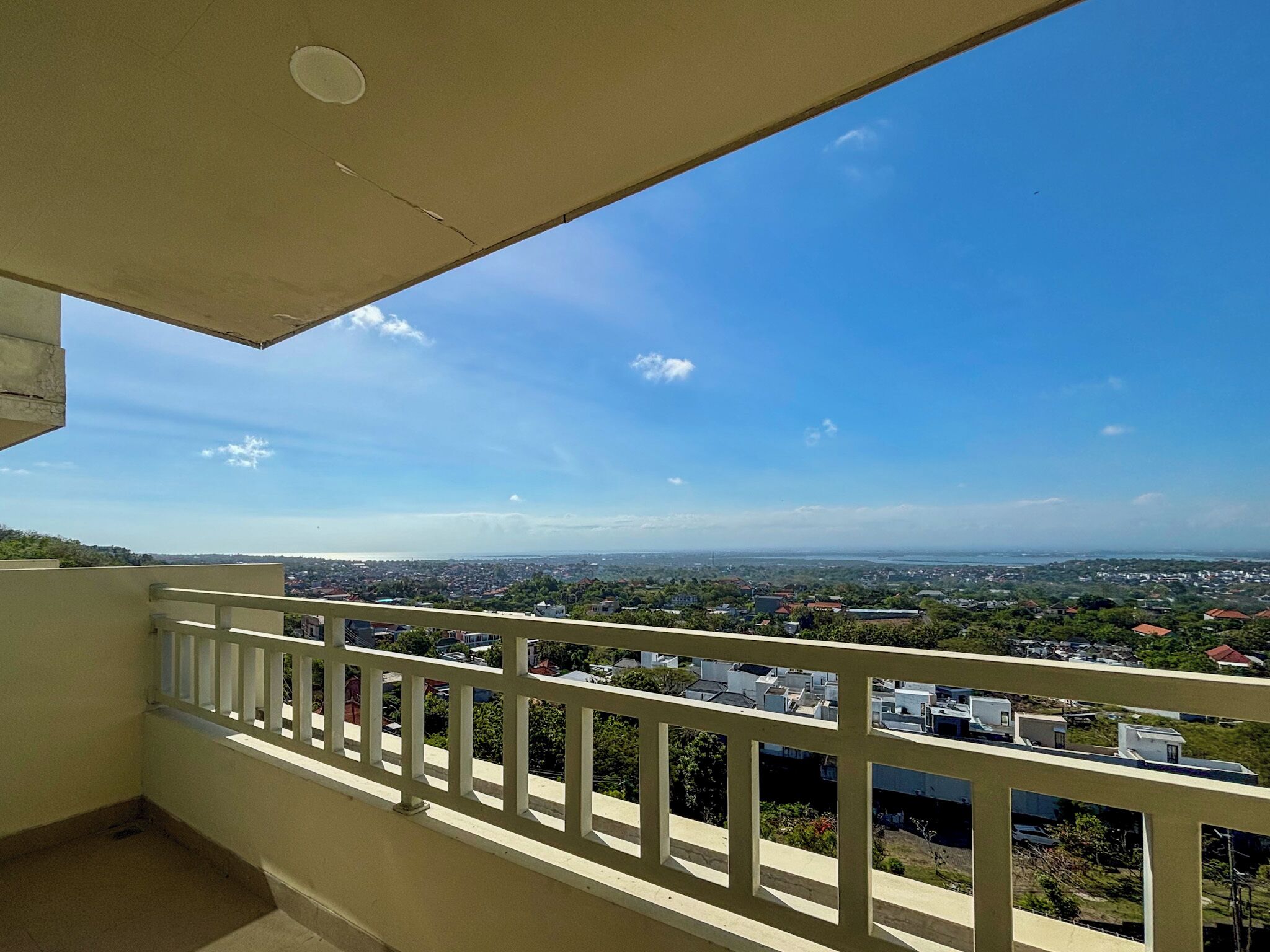 A balcony with a view of a cityscape, including buildings and greenery.