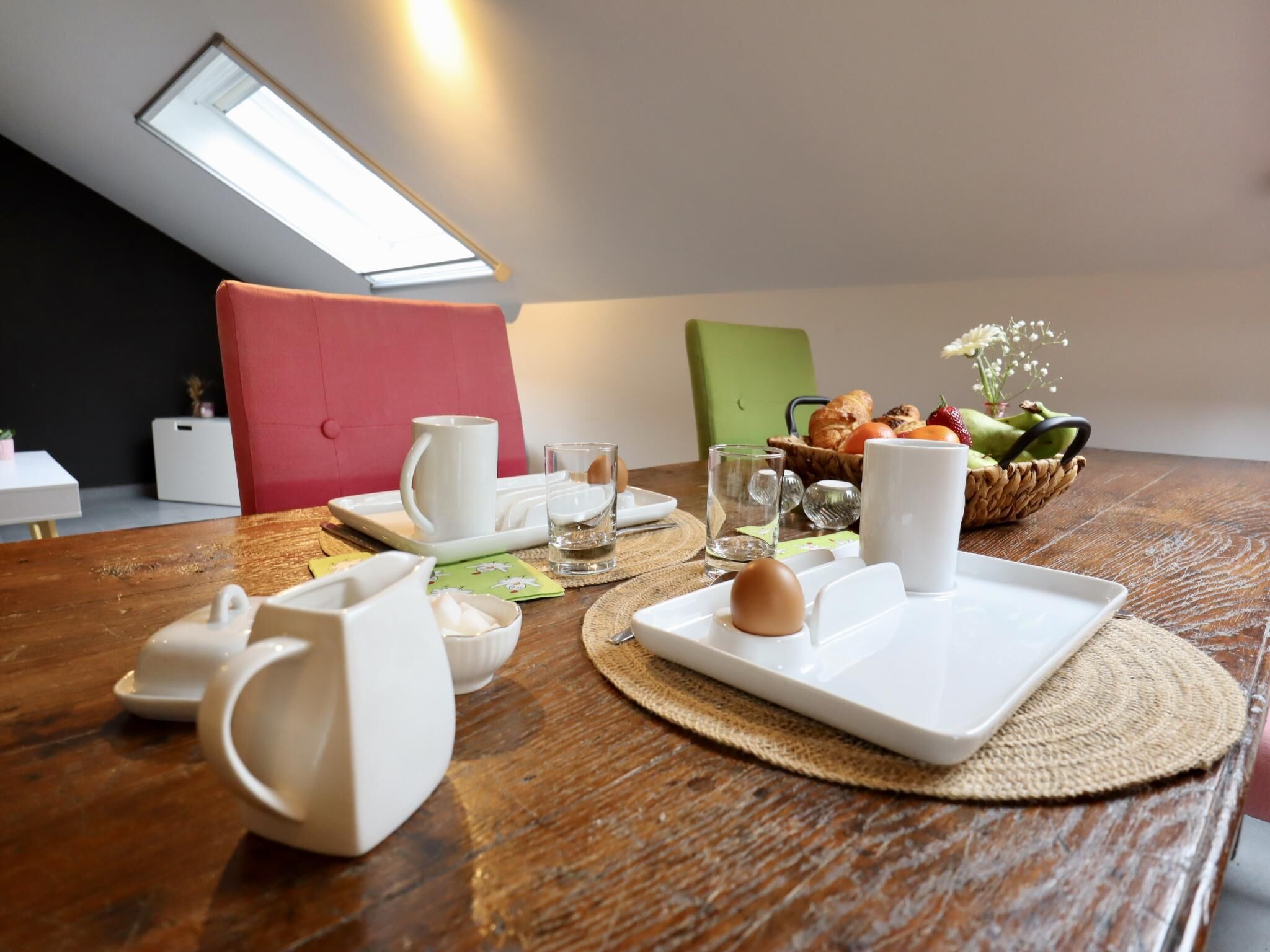 A dining table with breakfast items, a red chair, a green chair, and a small white table in the background.