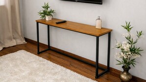A room with a mounted TV, a wooden console table, a remote control, a small potted plant, and a white rug.