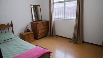 Een slaapkamer met een bed, een kaptafel, een nachtkastje, een spiegel en een raam met gordijnen.