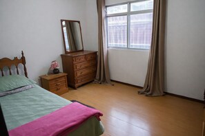 A bedroom with a bed, a dresser, a nightstand, a mirror, and a window with curtains. - Spacious house with garage, 3 bedrooms, ideal for families, 10 minutes from the city center. (Petrópolis)