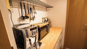 A compact kitchen with a coffee machine, microwave, and utensils on a rack.