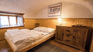 A bedroom with a wooden bed, a nightstand, a cabinet, a window with curtains, and a wall-mounted lamp.