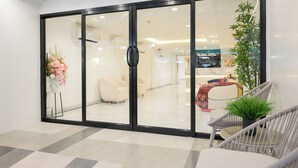 A modern hotel lobby with a glass door entrance, a potted plant, and a seating area with a sofa and chairs. - Global Hotel Pratunam Bangkok (Bangkok)