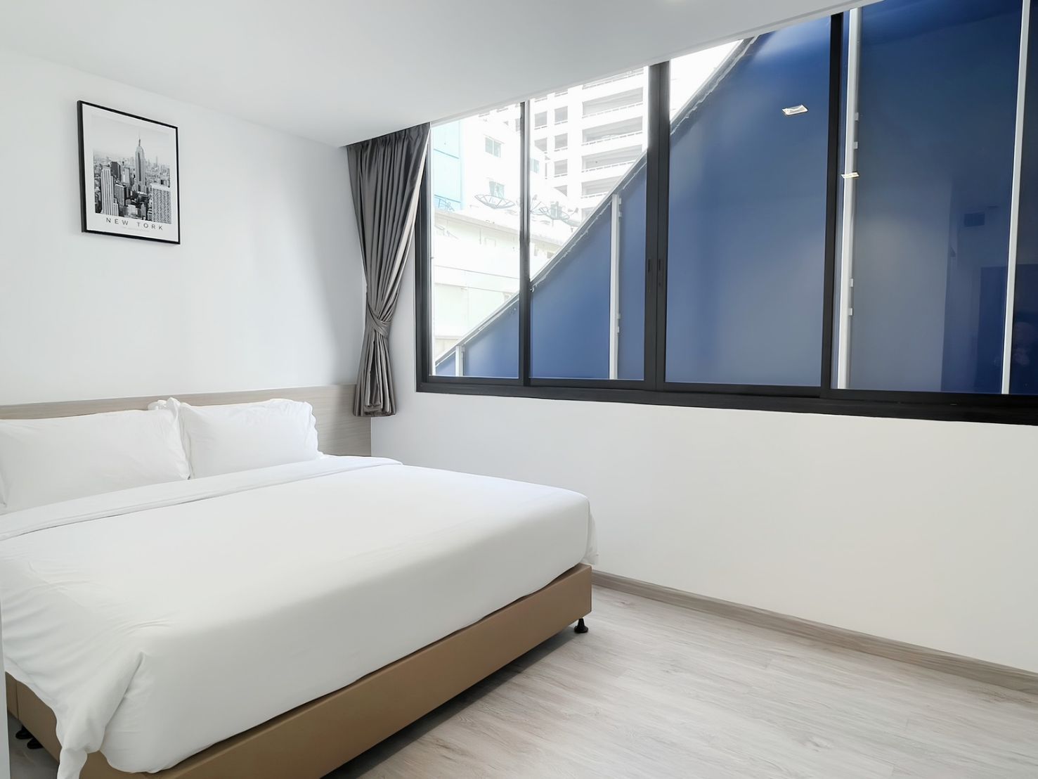 A hotel room with a large bed, a window with blue blinds, and a cityscape view.