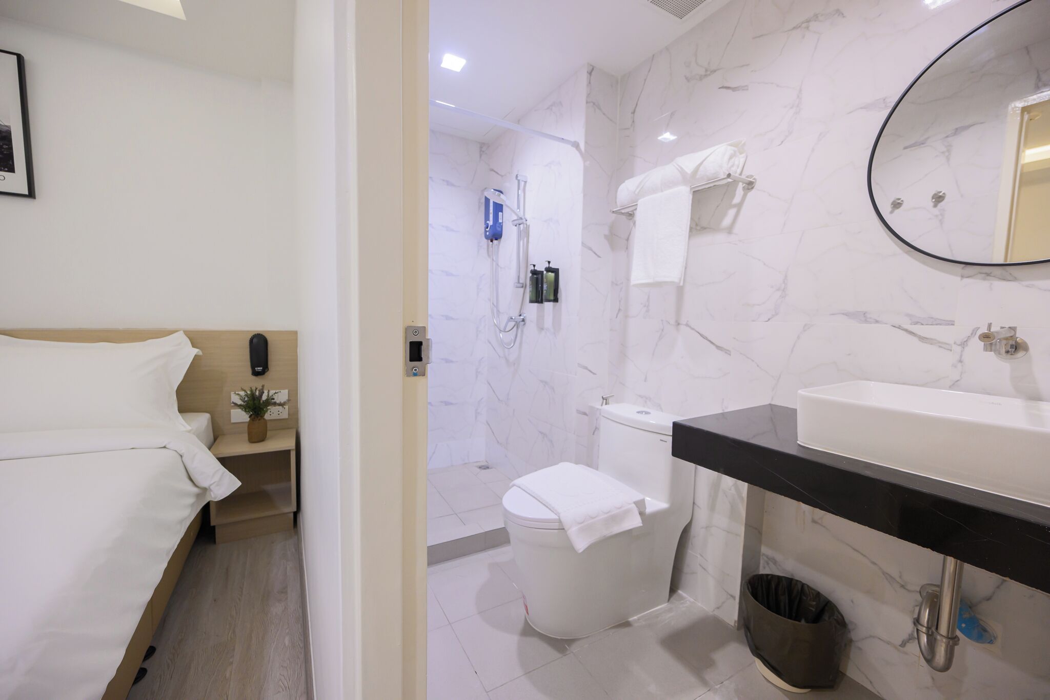 A modern bathroom with a marble wall, a white toilet, a black sink, and a shower area.