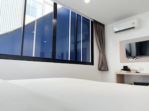 A hotel room with a large window, a flat-screen TV, a desk with a chair, and an air conditioning unit. - Global Hotel Pratunam Bangkok (Bangkok)