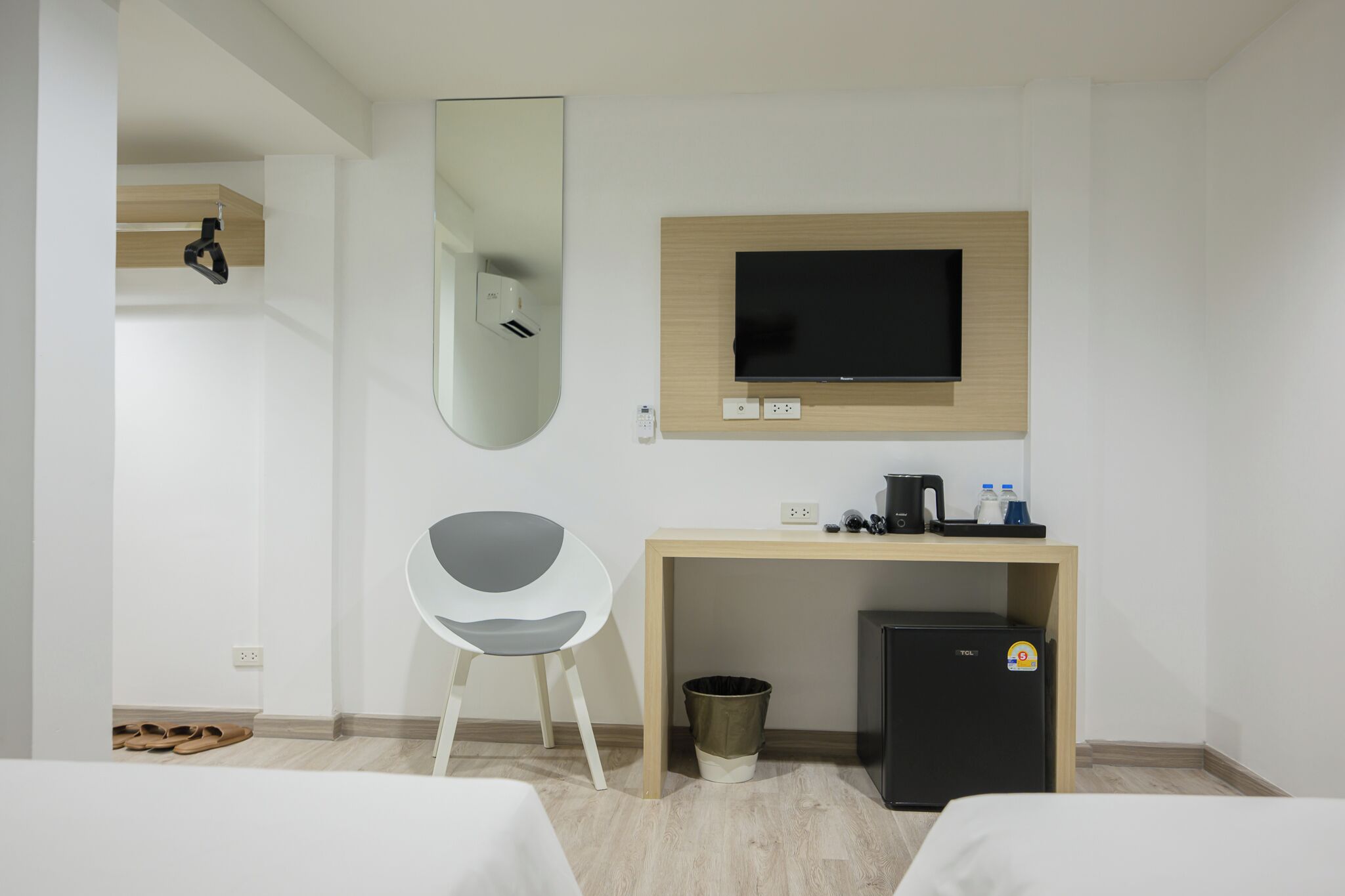 A hotel room with a bed, a desk with a TV, a chair, a trash bin, and a small refrigerator.