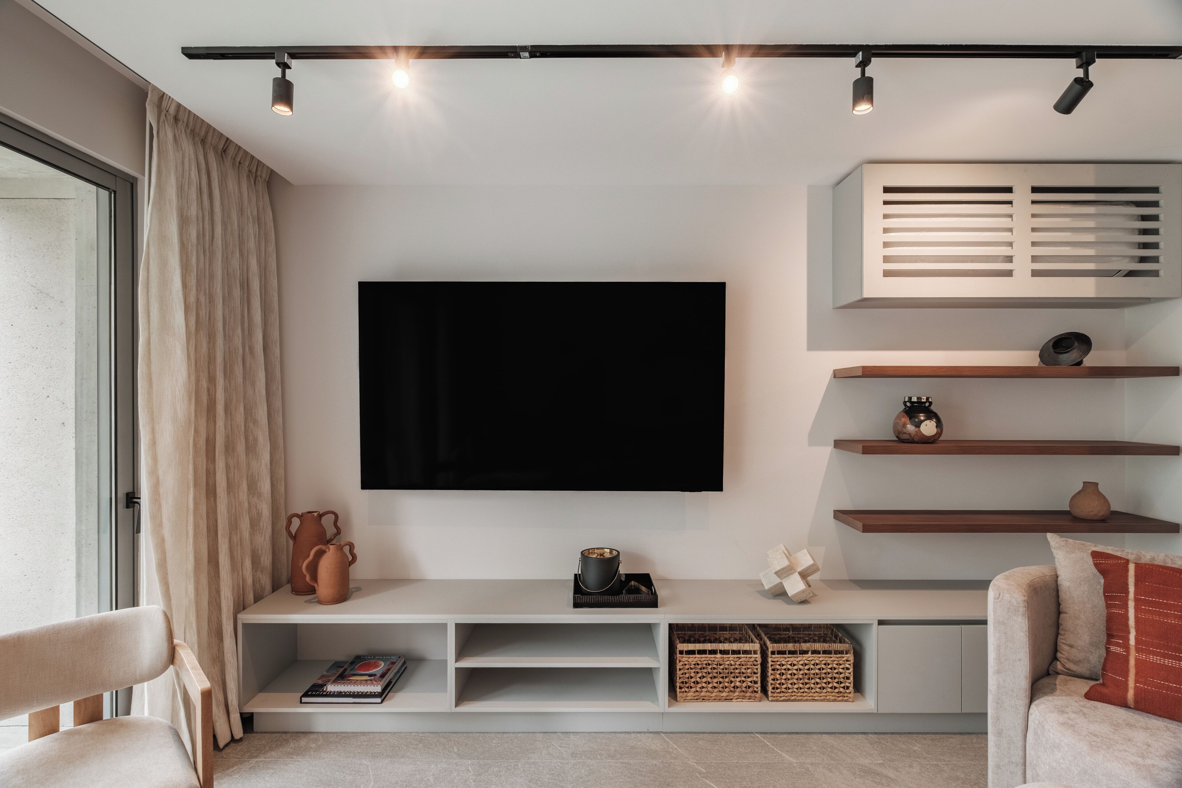 Una sala de estar moderna con un televisor de pantalla plana montado en la pared, un sofá, una mesa de centro y una estantería con adornos.