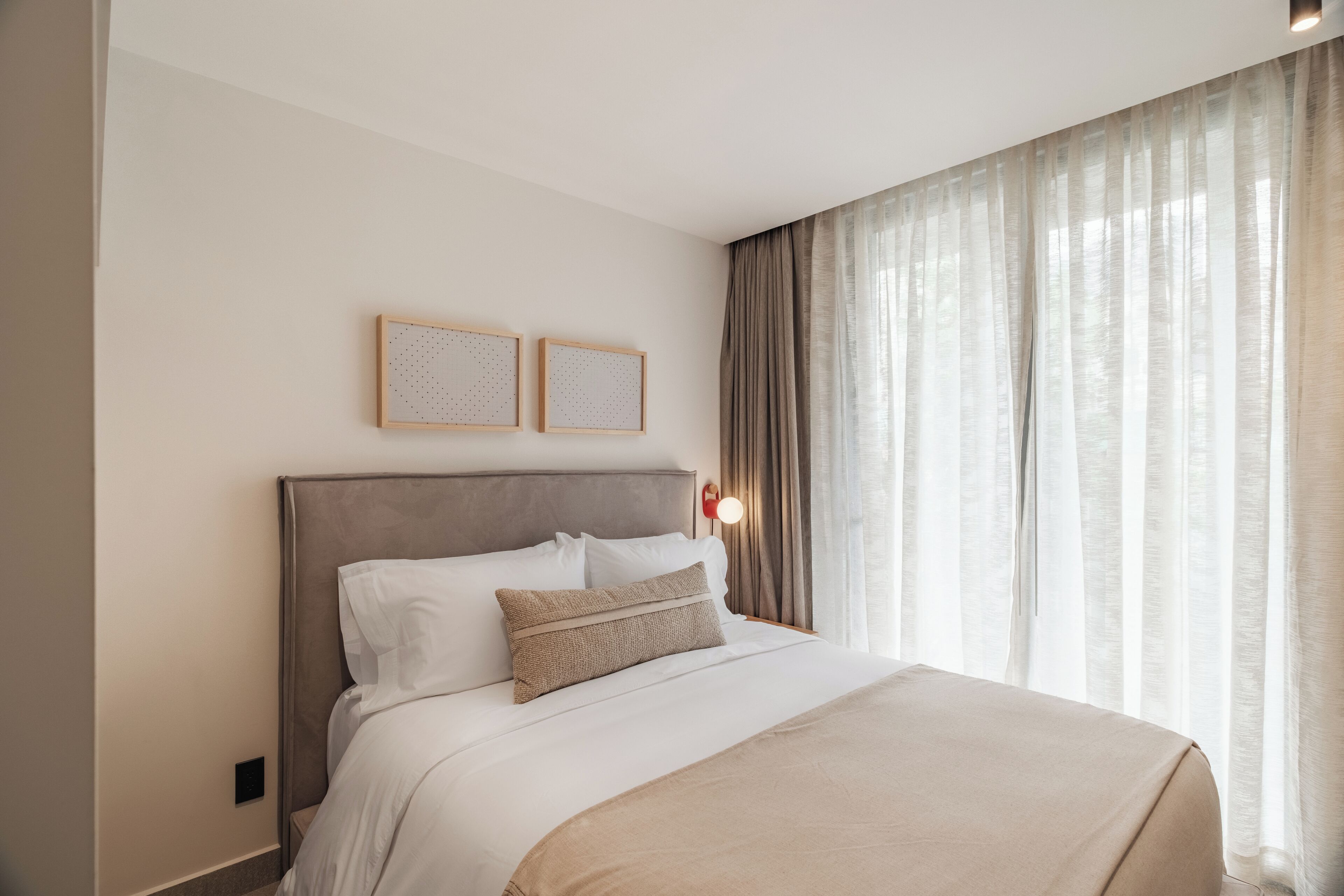 A neatly made bed with a headboard, two wall-mounted picture frames, and a bedside lamp.