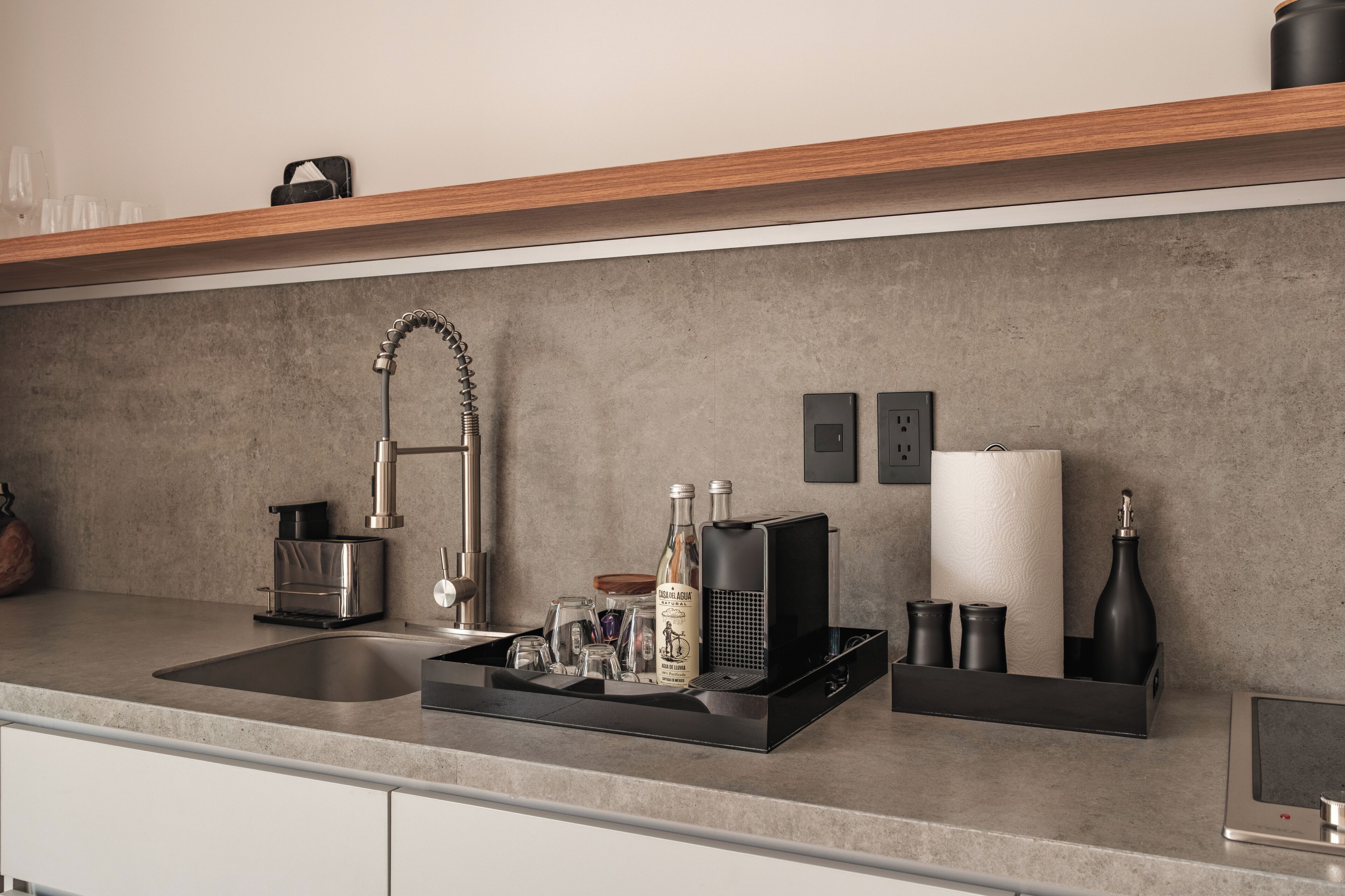 A modern kitchen with a stainless steel sink, a coffee machine, and a wine bottle on the counter.