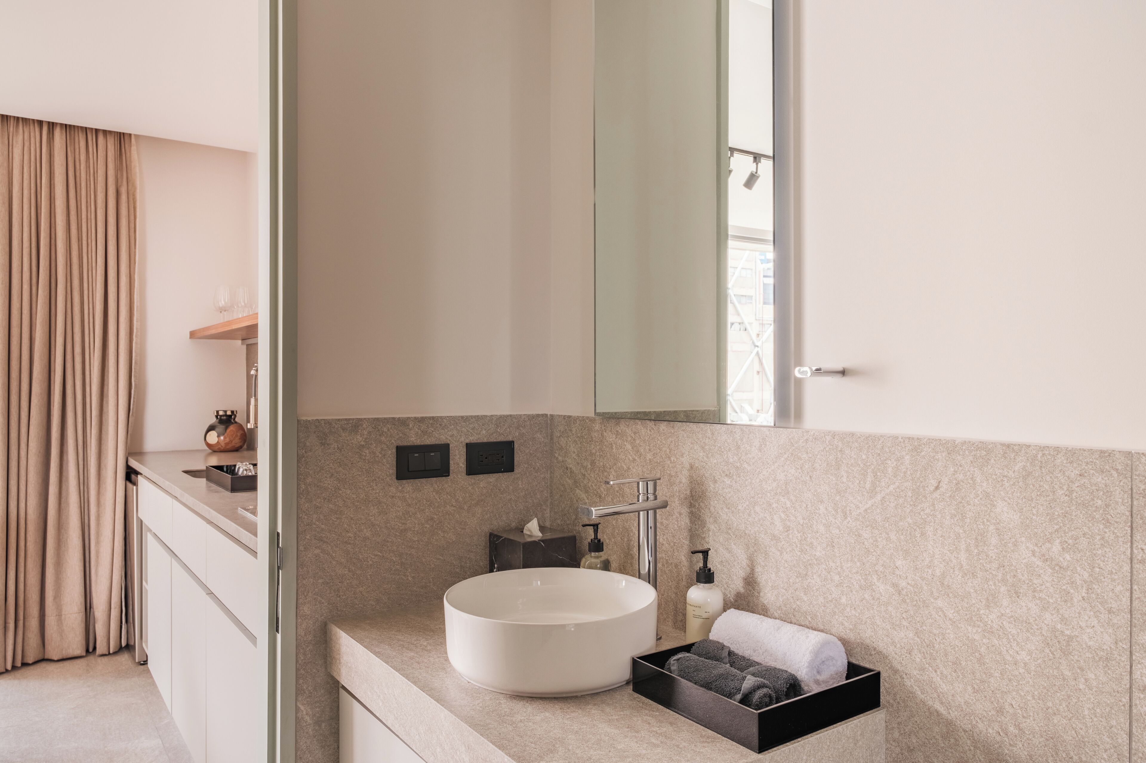 A modern bathroom with a round sink, a mirror, a towel rack, and a small shelf with toiletries.