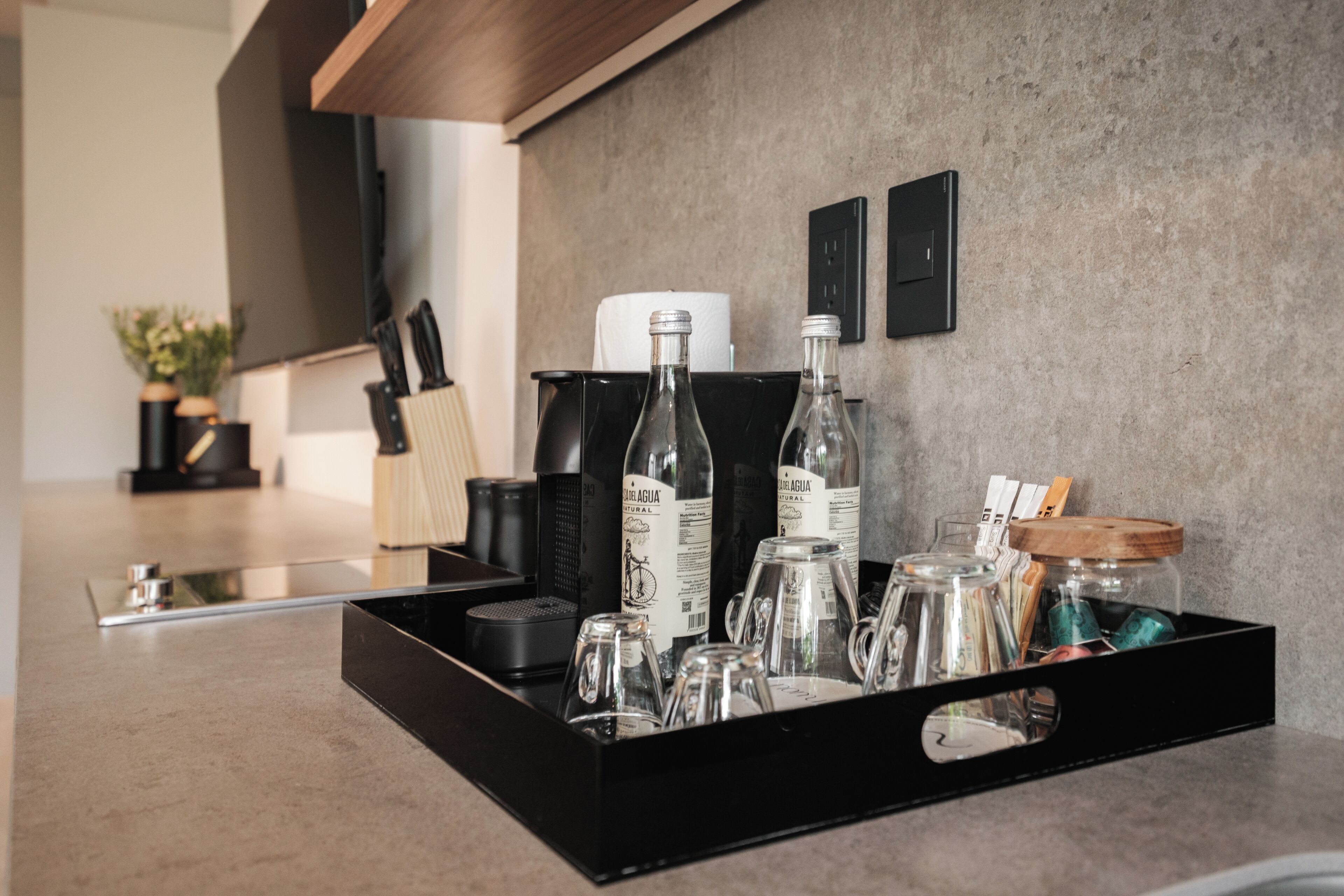 A kitchen counter with a tray holding various glass bottles, a coffee machine, and a knife set.