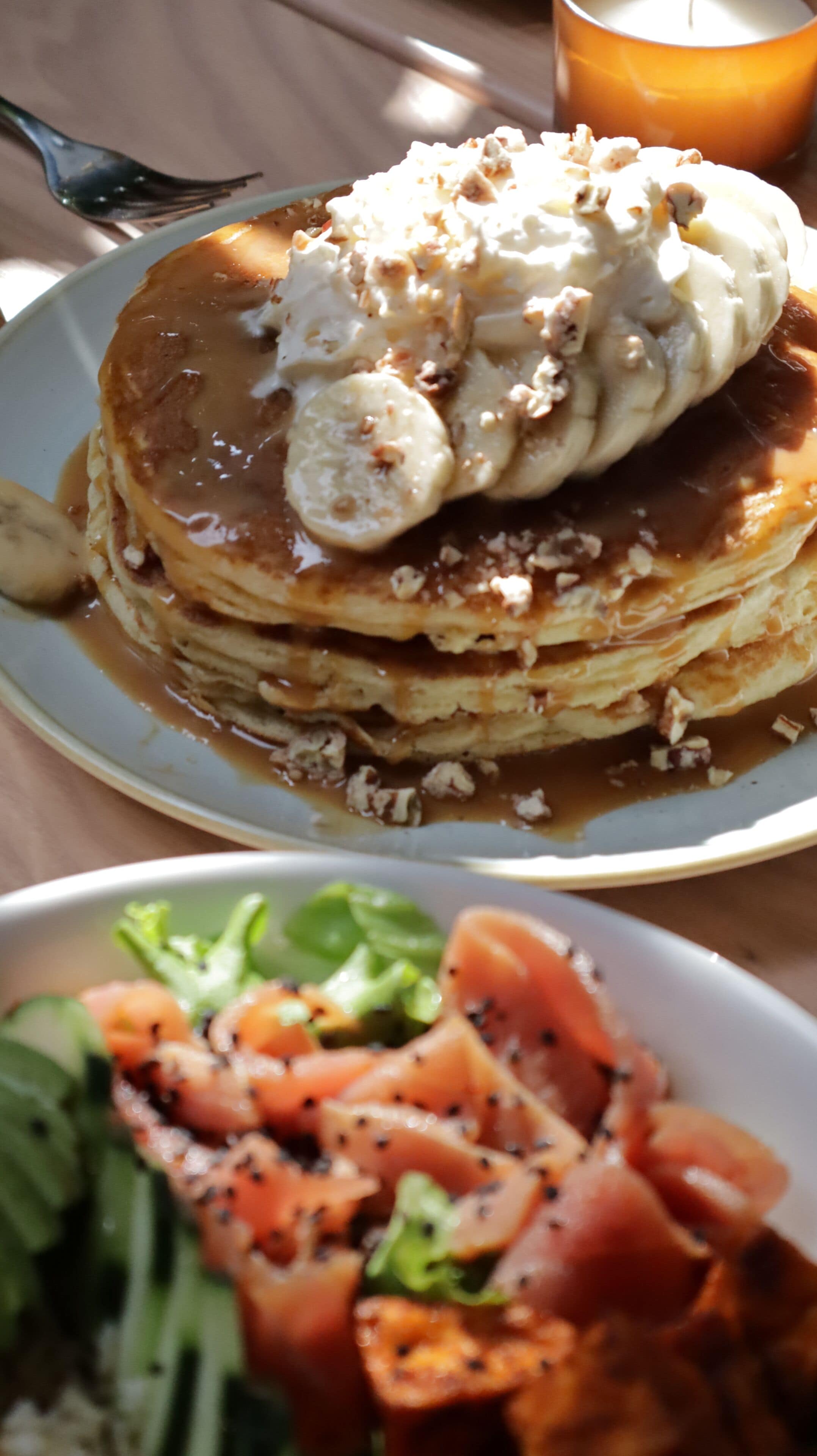 Een stapel pannenkoeken met toppings, een bord met groenten en een kaars op een tafel.