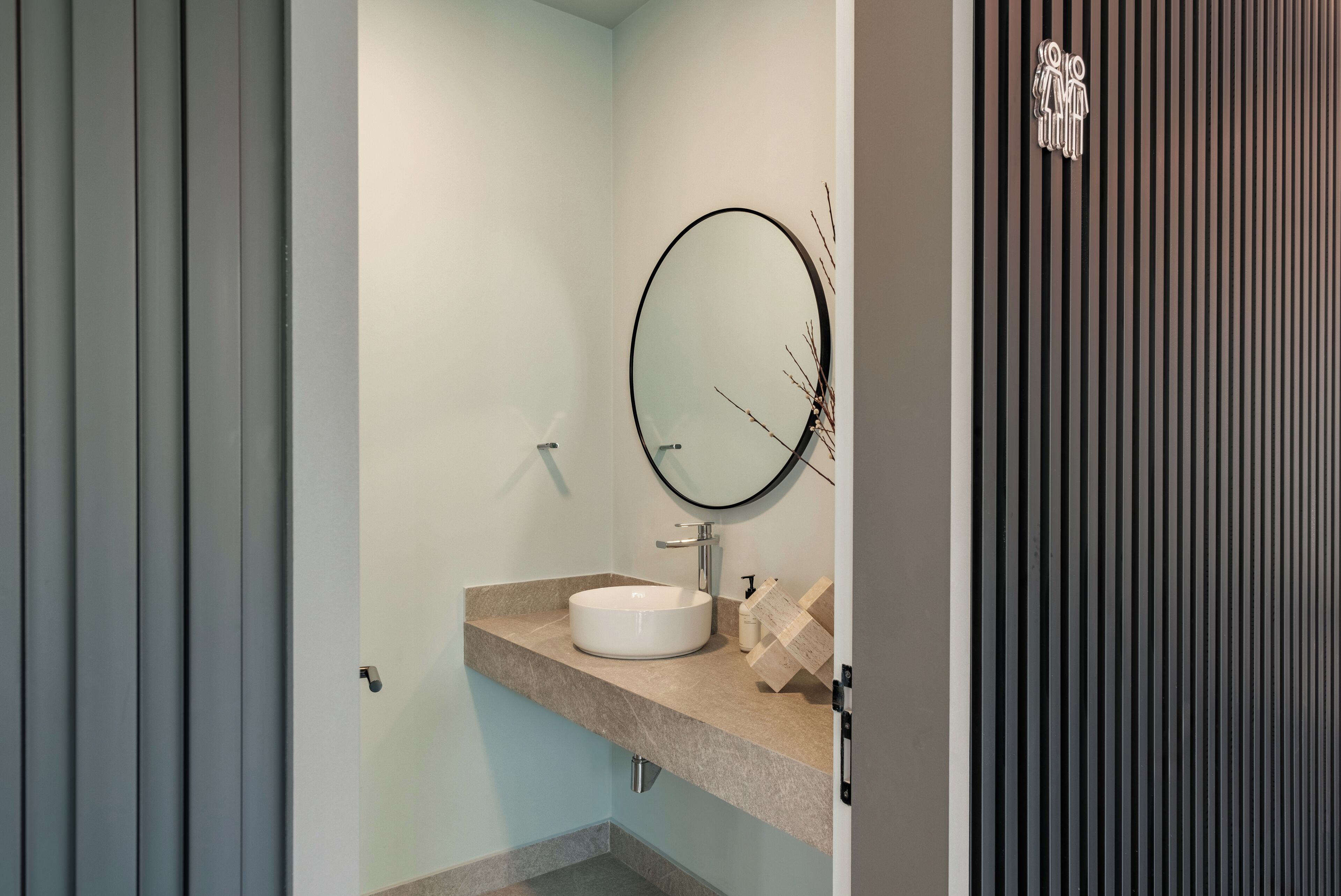 Een badkamer met een ronde spiegel, een wit wastafelmeubel en een handdoekrek.