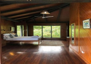 A room with a bed, a ceiling fan, and large windows.