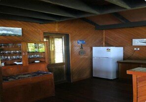 A wooden interior with a refrigerator, a wooden cabinet with glassware, and a door with a sign.
