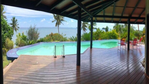 Eine Holzterrasse mit Blick auf einen Swimmingpool und den Ozean.