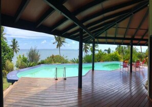Eine Holzterrasse mit Blick auf einen Swimmingpool und den Ozean.