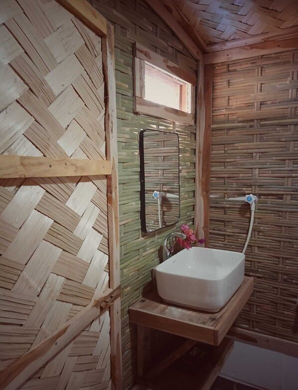 A bathroom with a woven wall design, a mirror, a sink, and a window. - Nisarga Pod House Kaptai (Rajasthali)