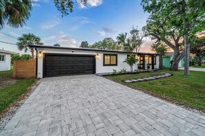 A modern single-story house with a paved driveway, garage, and a small garden area. - Cocoa Beach 4BR/2BA Retreat w Heated Pool (Cocoa Beach)