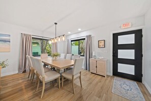 A dining area with a wooden table, chairs, and a chandelier. There is a door with an exit sign, a cabinet, and a rug on the floor. - Cocoa Beach 4BR/2BA Retreat w Heated Pool (Cocoa Beach)