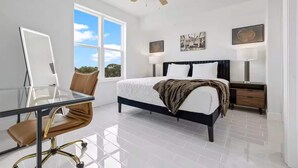 A bedroom with a bed, bedside tables, a desk, a chair, a ceiling fan, and large windows. - River Fly-In Duo - 5Bd - River & Runway View (Merritt Island)