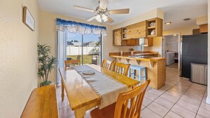 Un comedor con mesa y sillas de madera, ventilador de techo y vistas al exterior.