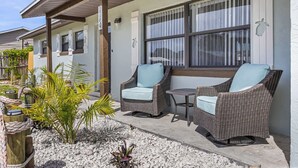 Un patio techado con mobiliario de mimbre, una pequeña mesa y una ventana con persianas.
