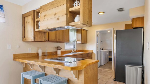 Una cocina con armarios de madera, un refrigerador de acero inoxidable e isla de madera con taburetes.