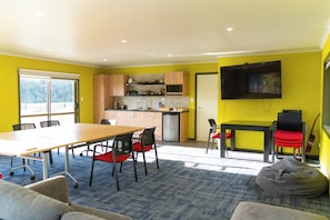 A modern kitchen with a flat-screen TV, a dining area with a table and chairs, and a bean bag in a room with yellow walls. - Timber Trail Lodge & Transport (Piropiro)