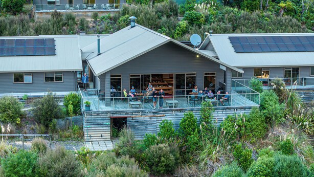 A modern house with a deck, solar panels, and a lush garden. - Timber Trail Lodge & Transport (Piropiro)