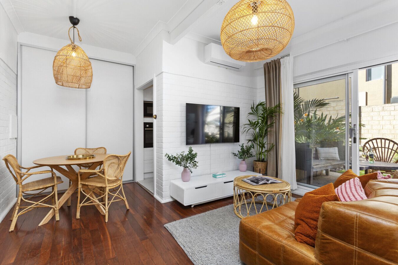 A modern living room with a dining area, a sofa, a TV, and a balcony with plants.