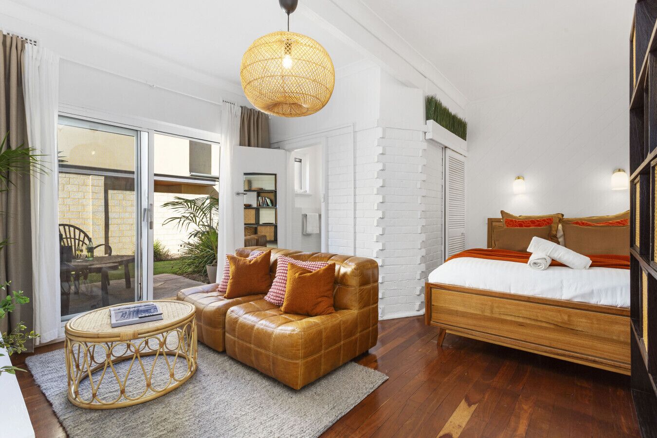 Une chambre d’hôtel moderne avec un canapé en cuir, une table ronde en osier, un lit avec une tête de lit en bois et une grande fenêtre donnant sur l’extérieur.