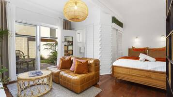 Une chambre d’hôtel moderne avec un canapé en cuir, une table ronde en osier, un lit avec une tête de lit en bois et une grande fenêtre donnant sur l’extérieur.