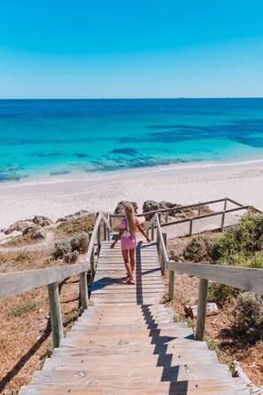 Una scala di legno che conduce a una spiaggia con acque cristalline blu.