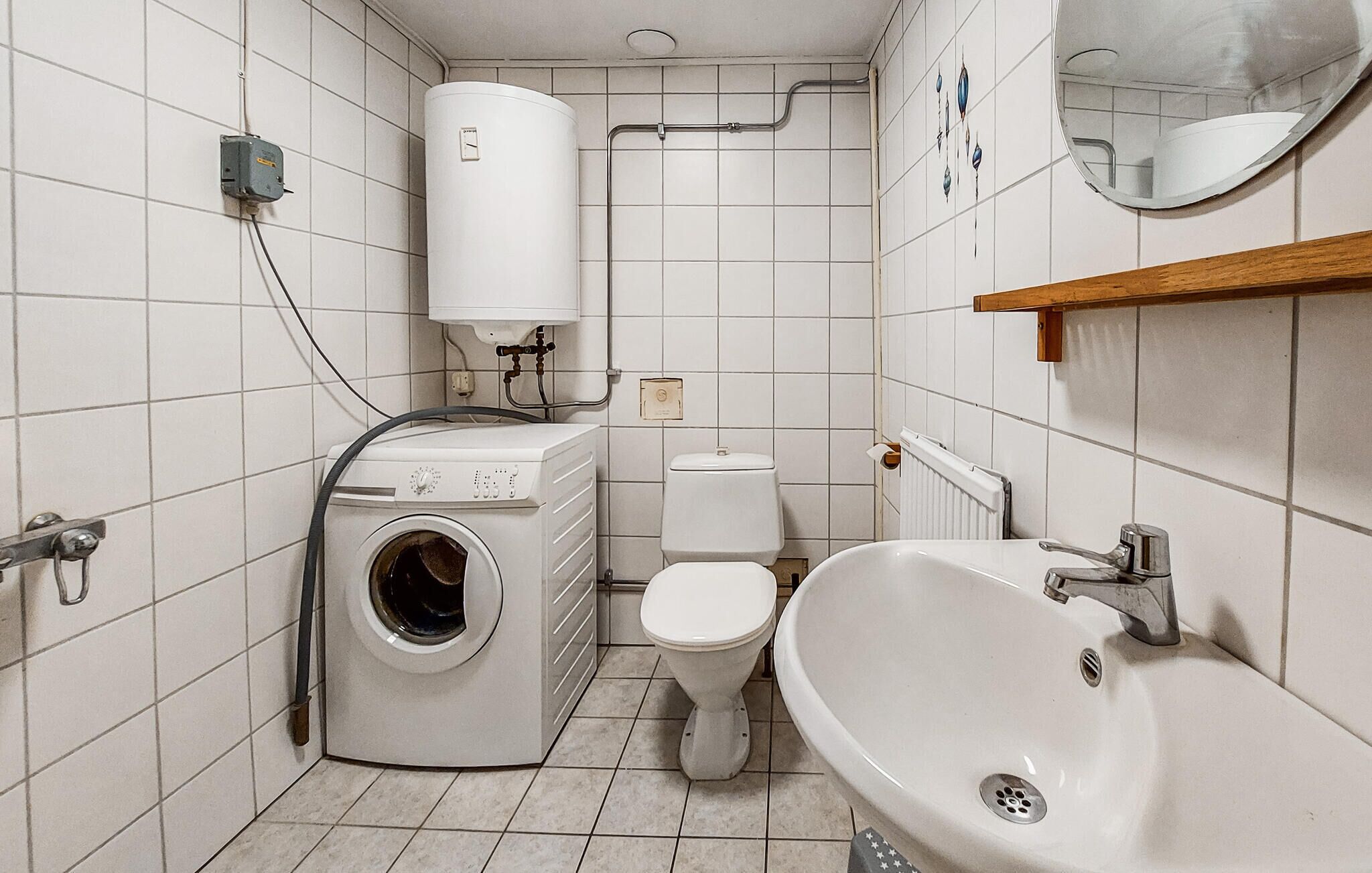A compact bathroom with a washing machine, toilet, sink, and a water heater.