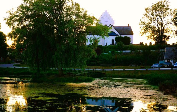 A serene riverside setting with a white building, a bridge, and lush greenery.