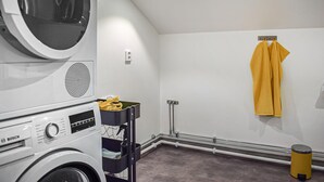 A laundry room with a Bosch washing machine, a drying rack, and a yellow trash bin.