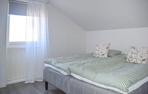A bedroom with a bed, a window with sheer curtains, and a radiator.