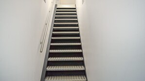 A narrow stairway with metal railings and patterned steps leading to a door.