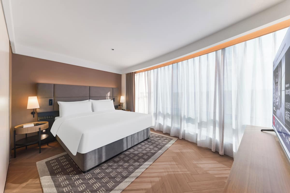 Een moderne hotelkamer met een groot bed, nachtkastjes, een televisie en een groot raam met gordijnen.