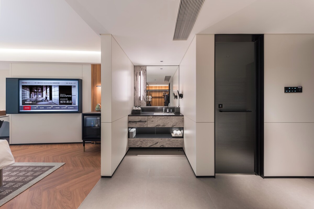 A modern hotel room with a large flat-screen TV, a sleek kitchen area, and a built-in refrigerator.