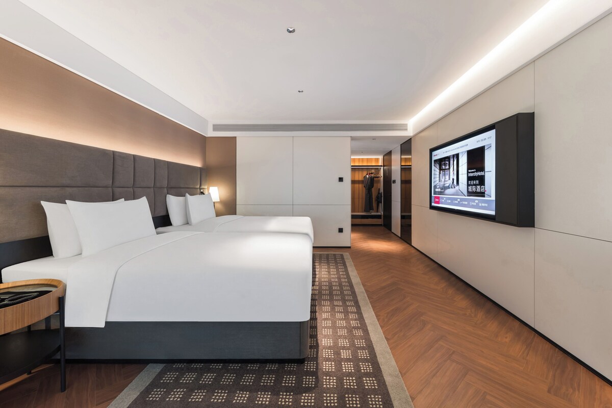 A modern hotel room with a large bed, a TV mounted on the wall, and a wooden floor.