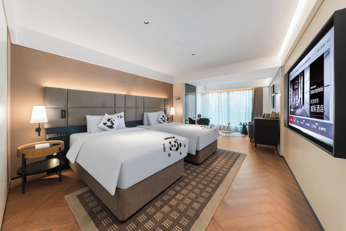 Een hotelkamer met twee bedden, een televisie, een bureau en uitzicht op de stad.