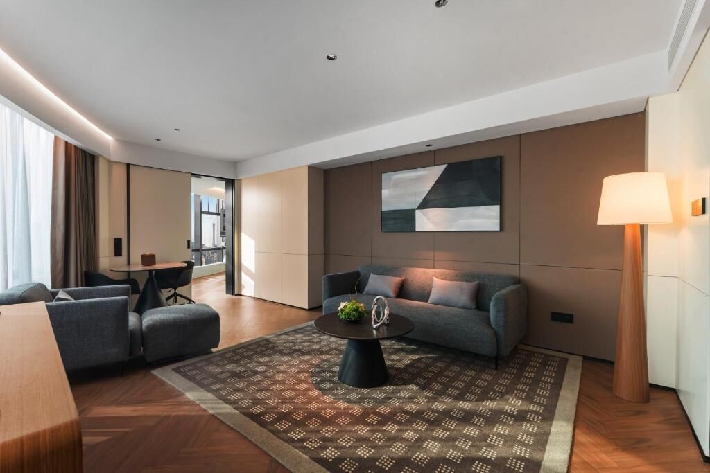 A modern hotel room with a sofa, a coffee table, a lamp, and a large abstract painting on the wall.