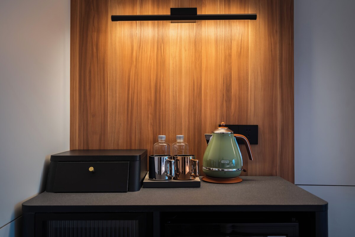 A kitchenette with a coffee maker, two bottles, and a kettle on a countertop.