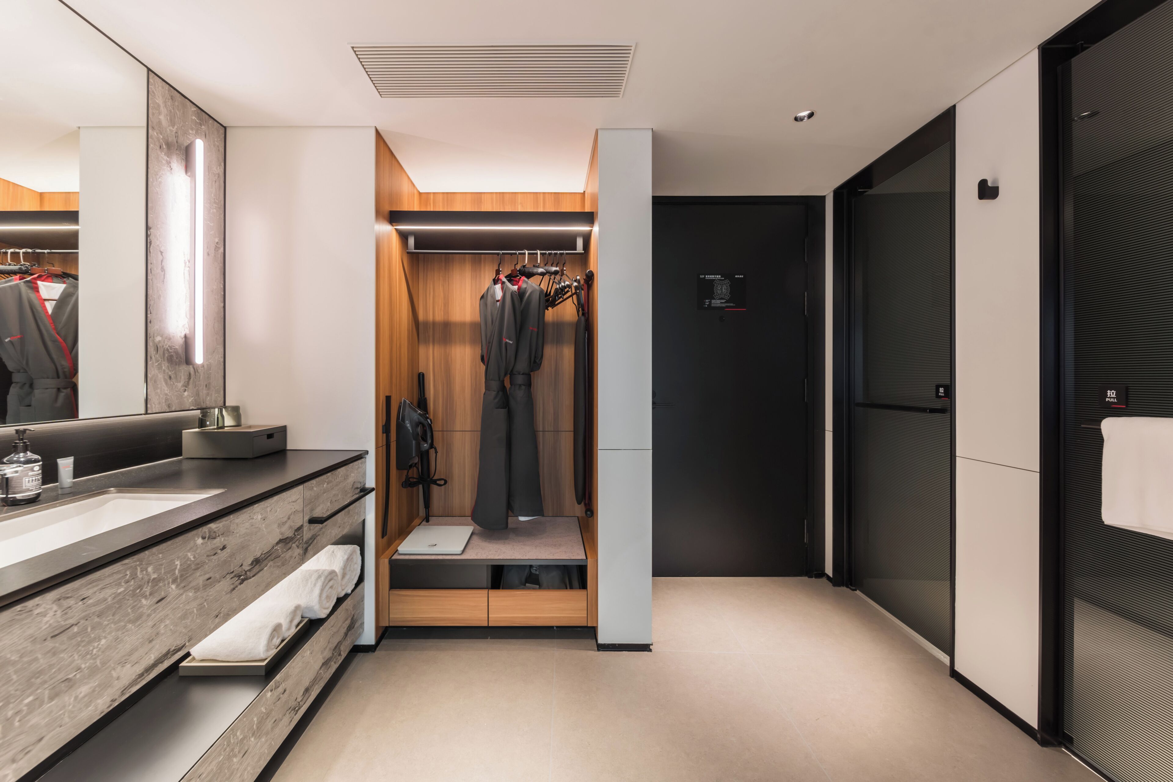 A modern bathroom with a large mirror, a wooden vanity, and a walk-in closet with hanging clothes.