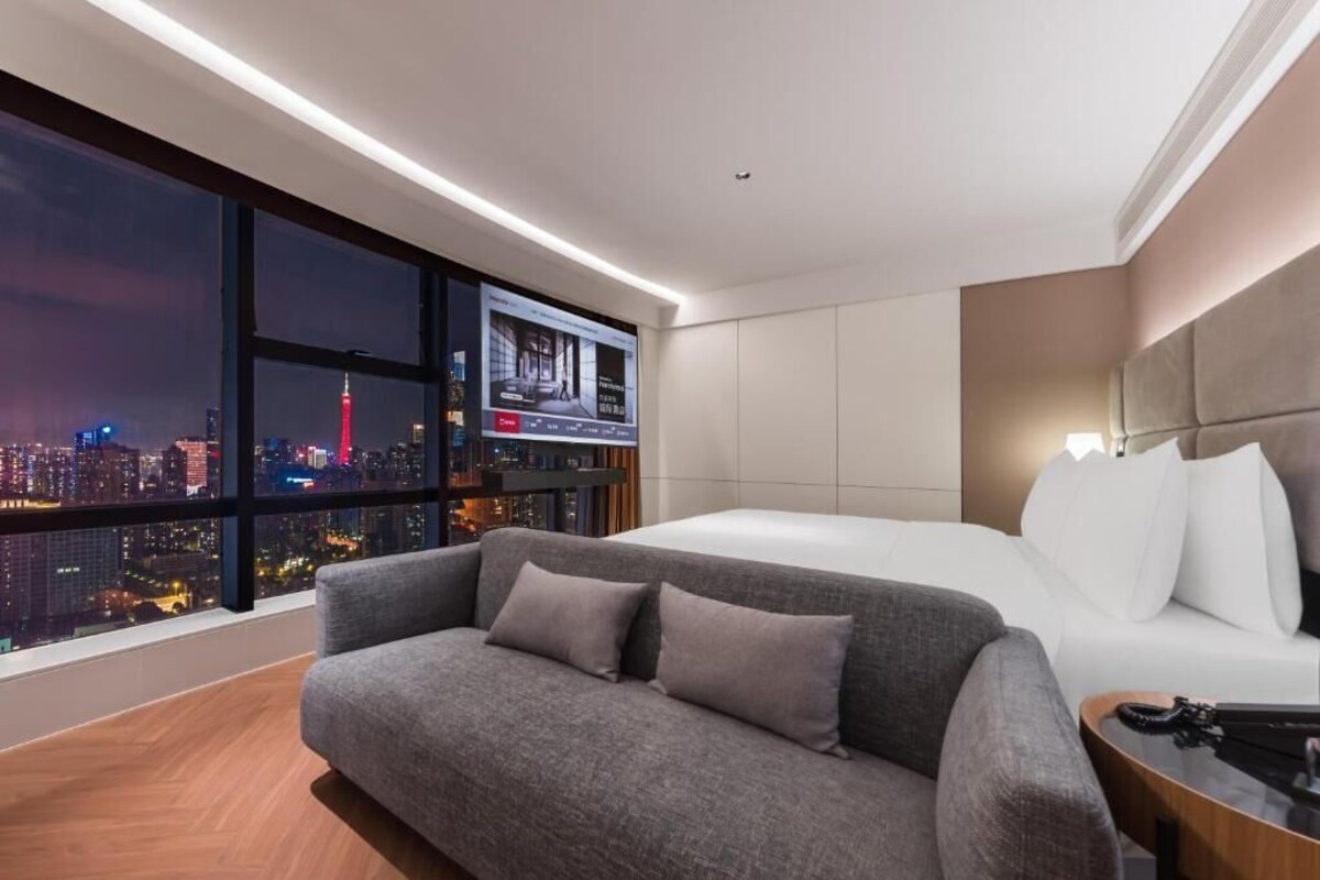 Een moderne hotelkamer met een groot raam, een bank, een bed en een televisie.