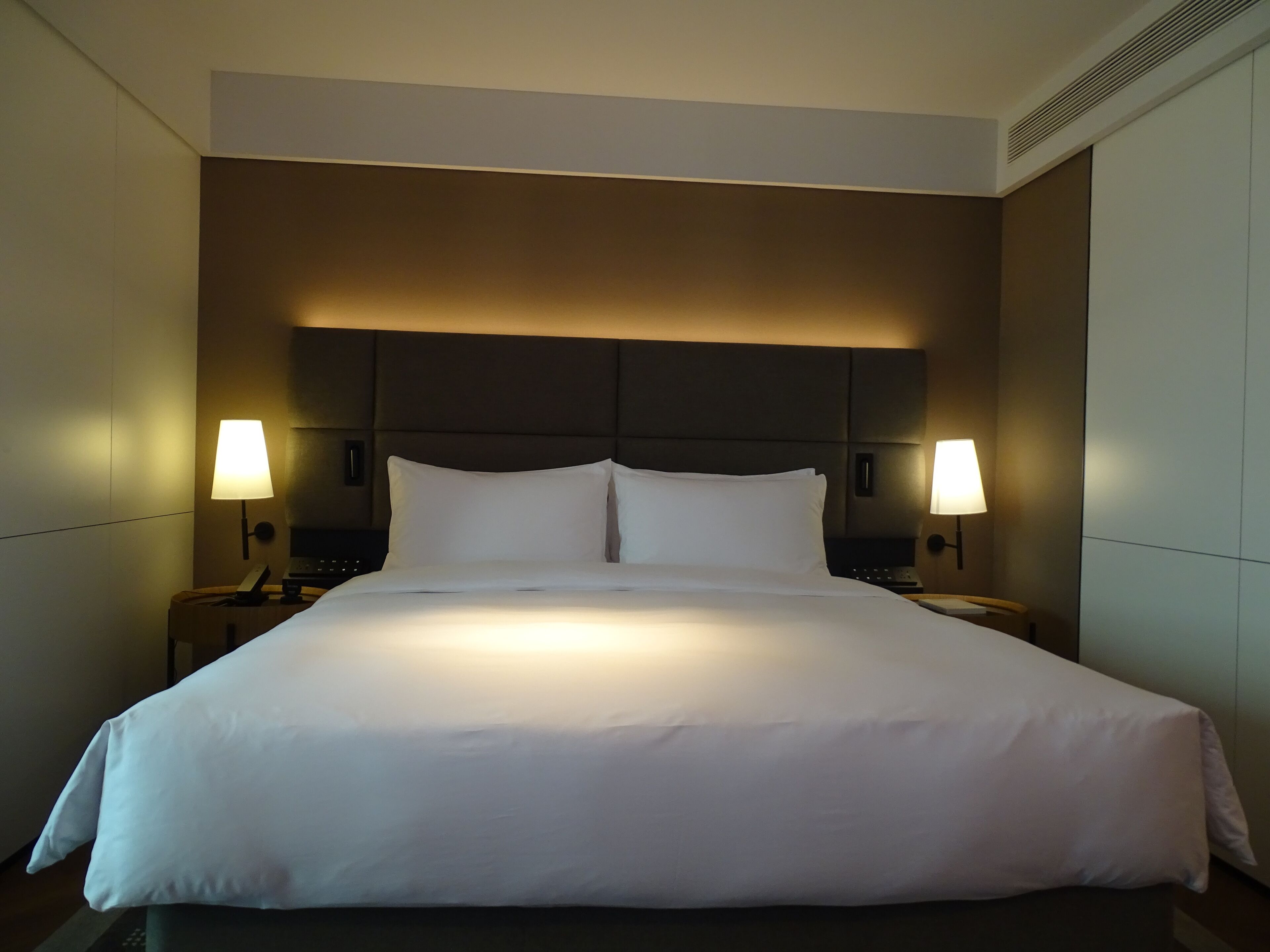 A hotel room with a large bed, two bedside lamps, and a headboard with built-in lighting.